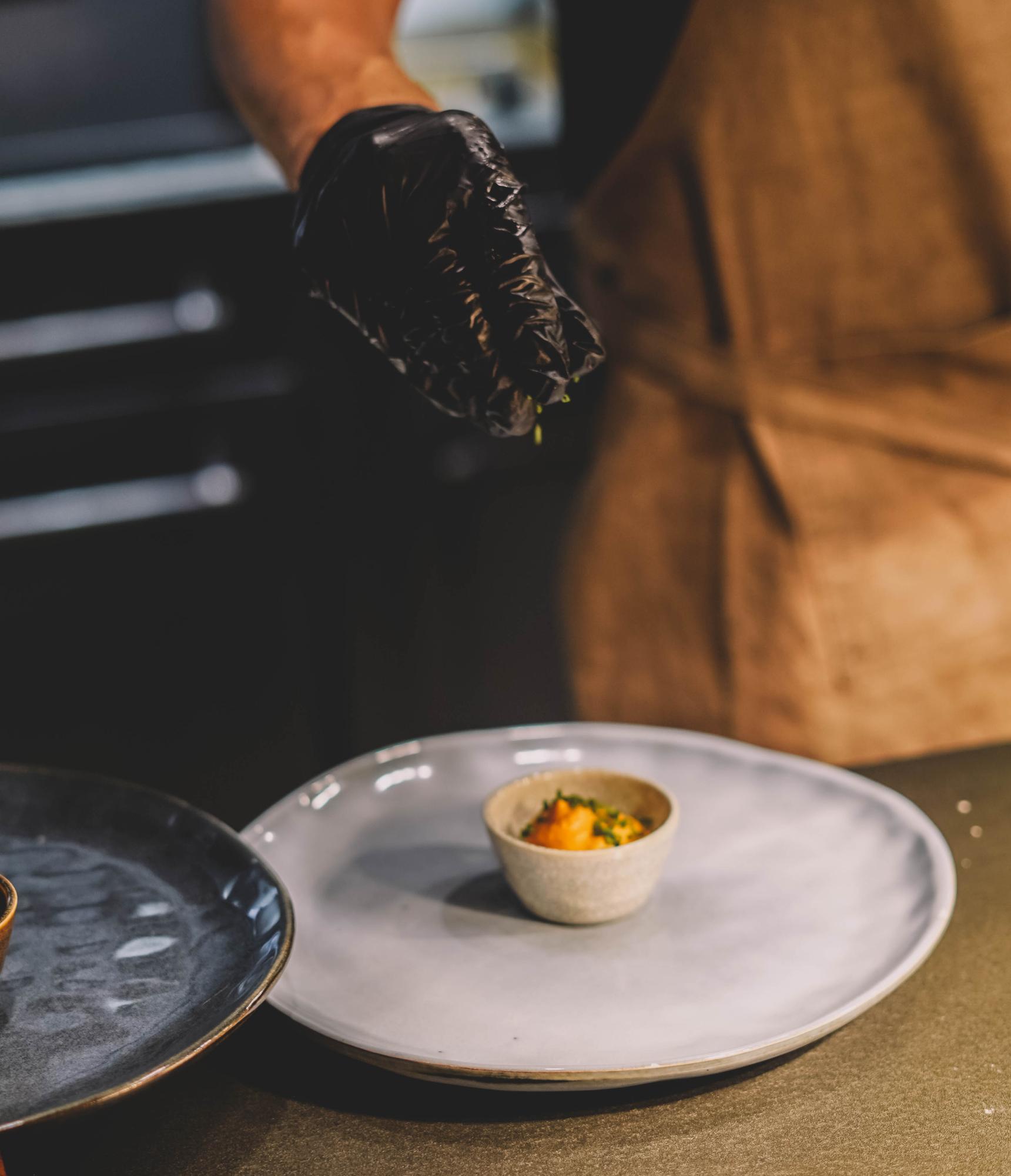 Chef plating a refined dish on dark plate